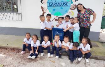 Young kids (around 15) with their teacher, in front of a building with a Carmeuse sign (earth with kids around and the logo of Carmeuse inside) and a Carmeuse flag